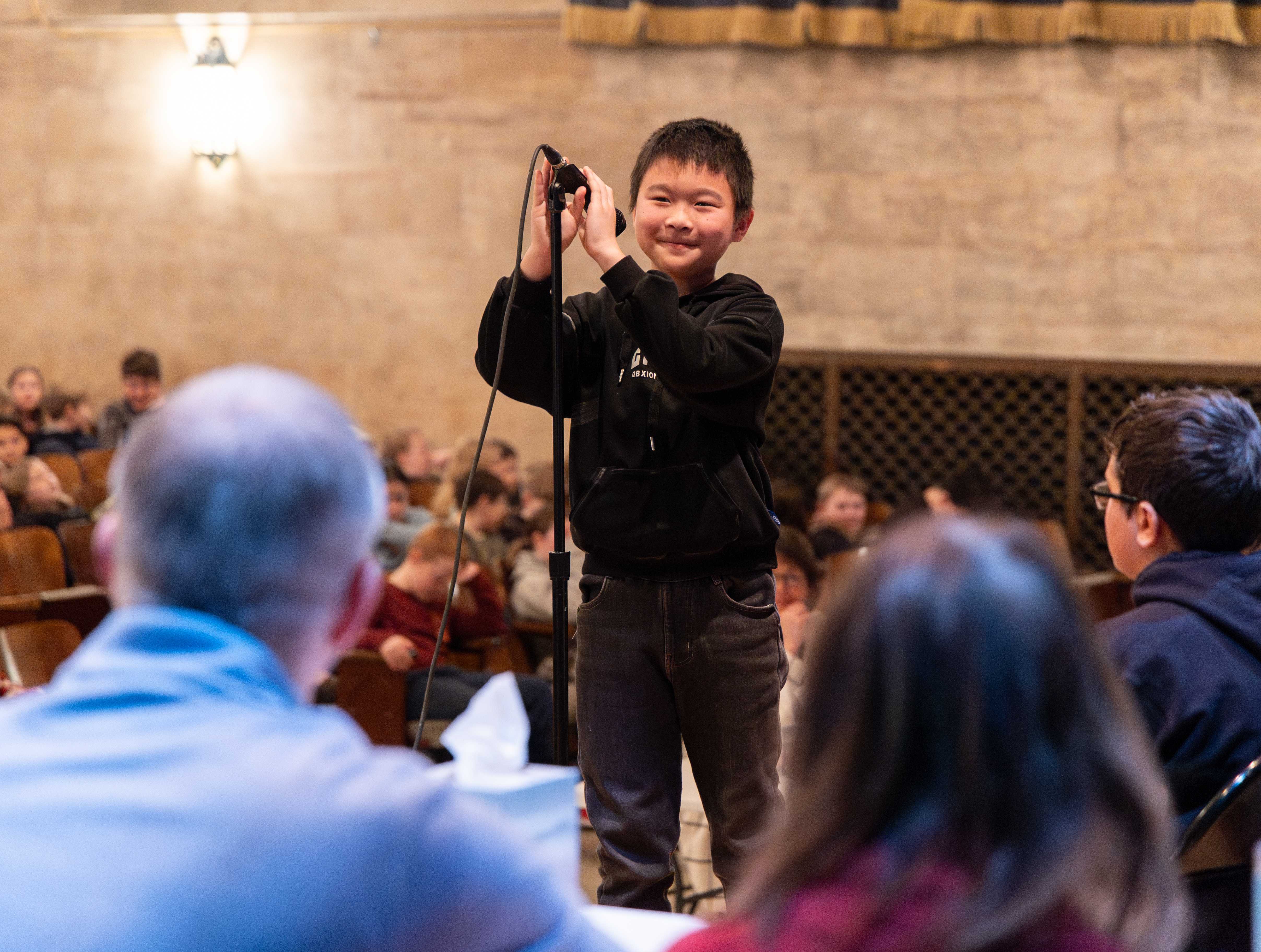 A student smiles as he spells a word at the microphone